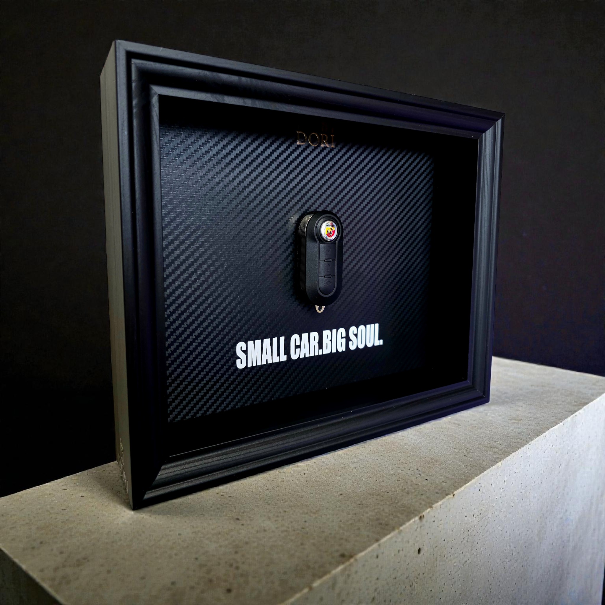 Automobilio raktelio dekoratyvinis paveikslas su anglies pluošto fonu ir užrašu „Small Car. Big Soul.“