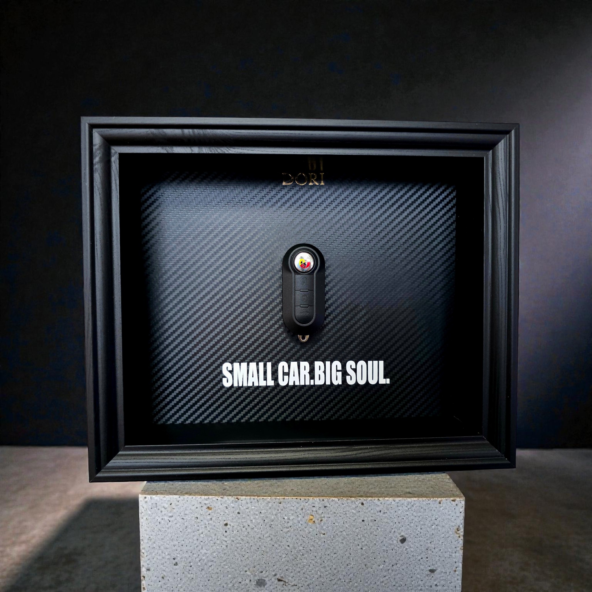 Automobilio raktelio dekoratyvinis paveikslas su anglies pluošto fonu ir užrašu „Small Car. Big Soul.“