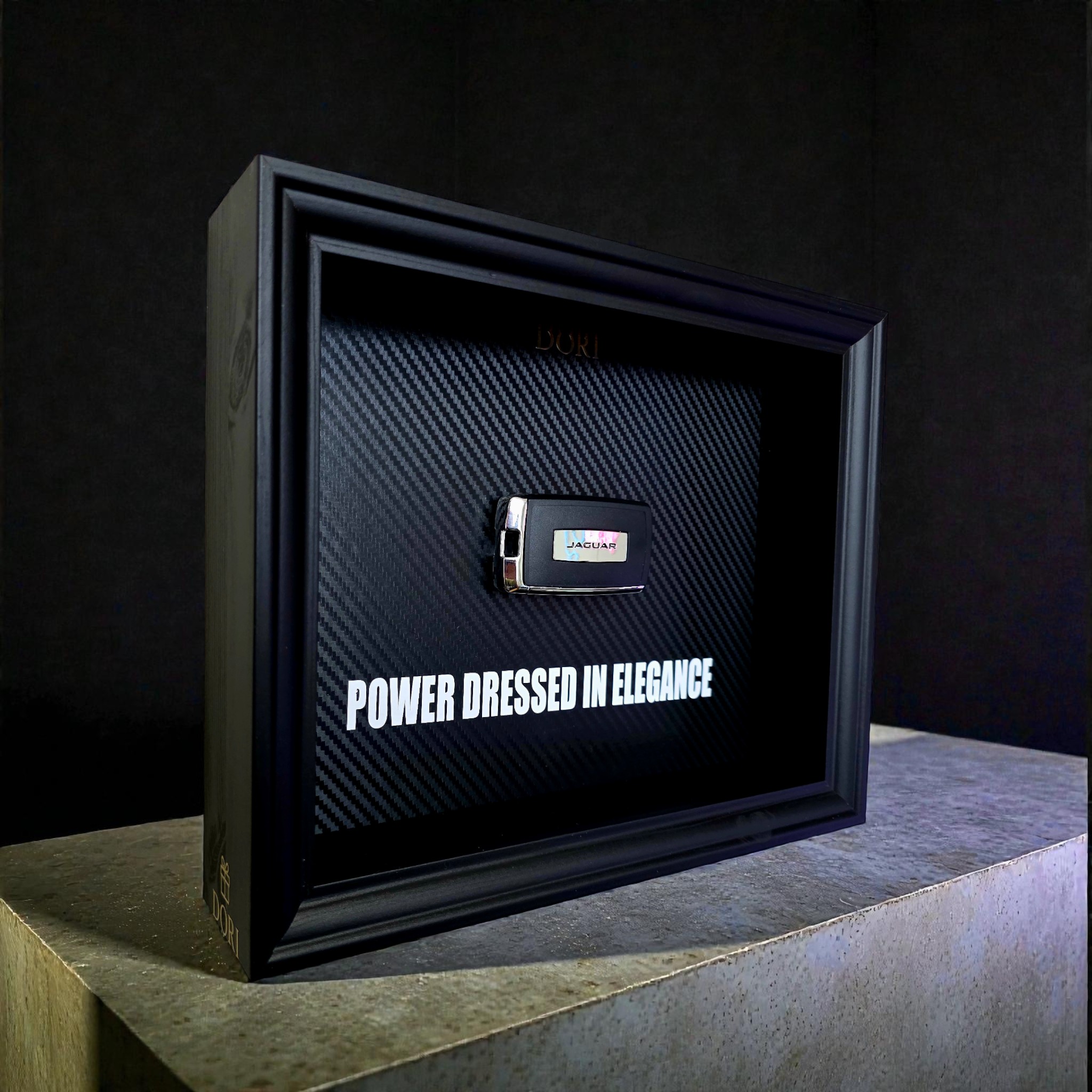 Automobilio raktelio dekoratyvinis paveikslas su anglies pluošto fonu ir užrašu „Power Dressed in Elegance“