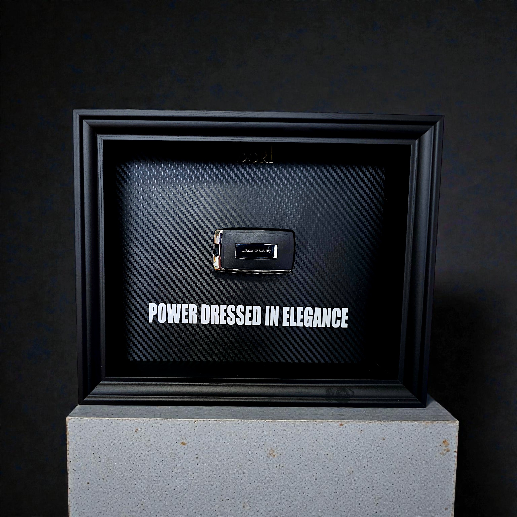 Automobilio raktelio dekoratyvinis paveikslas su anglies pluošto fonu ir užrašu „Power Dressed in Elegance“