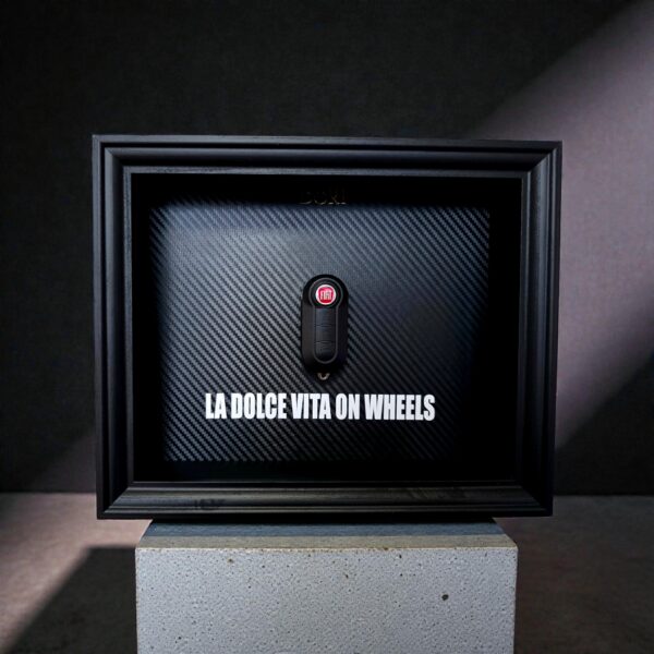 Automobilio raktelio dekoratyvinis paveikslas su anglies pluošto fonu ir užrašu „La Dolce Vita on Wheels“