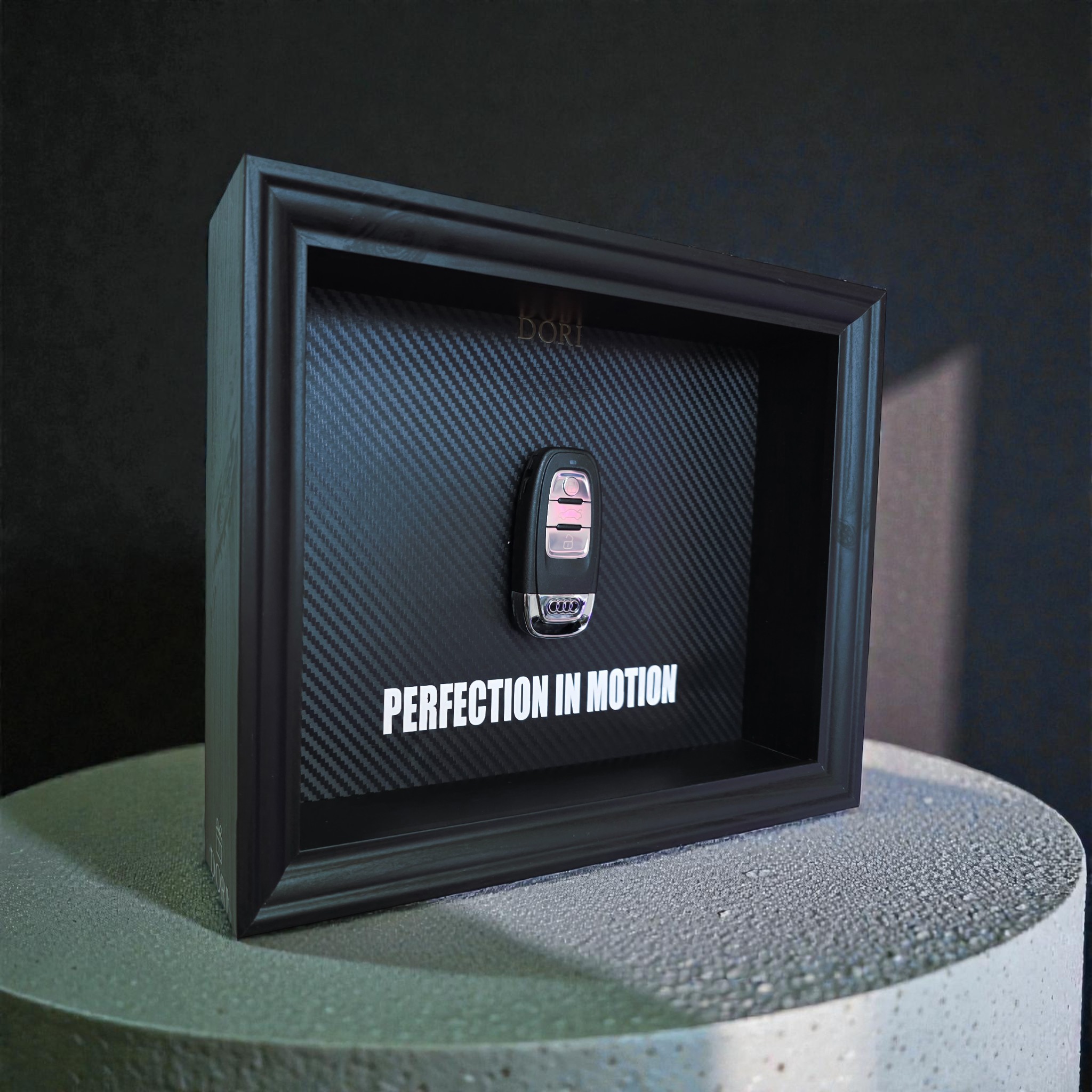 Automobilio raktelio meno paveikslas rėmelyje su anglies pluošto fonu ir užrašu „Perfection in Motion“