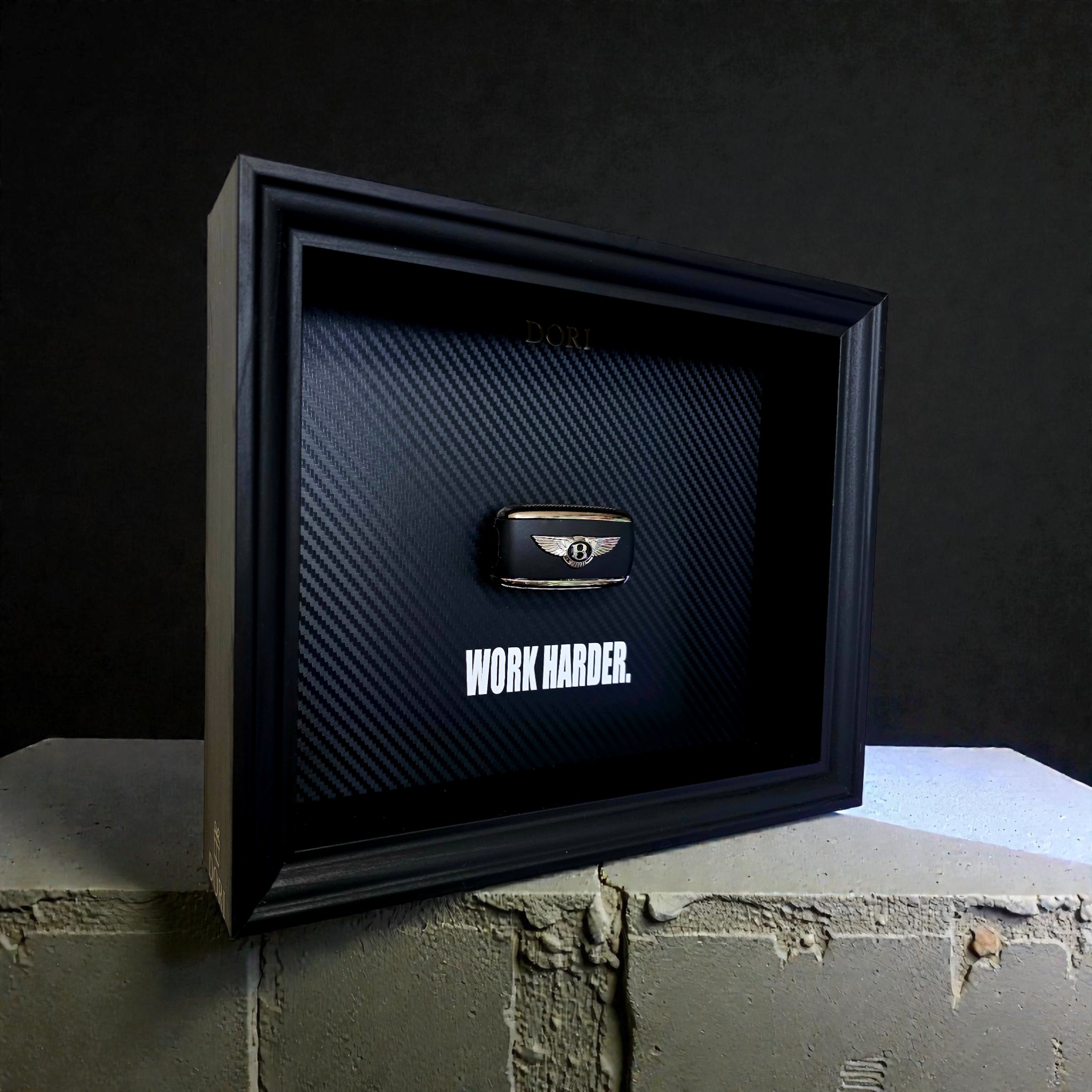 Automobilio raktelio dekoratyvinis paveikslas su anglies pluošto fonu ir užrašu „Work Harder“