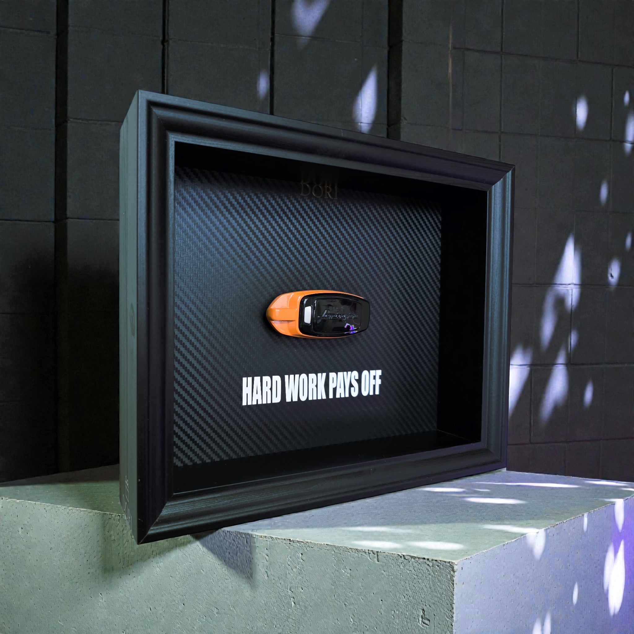 Automobilio raktelio dekoratyvinis paveikslas su anglies pluošto fonu ir užrašu „Hard Work Pays Off“