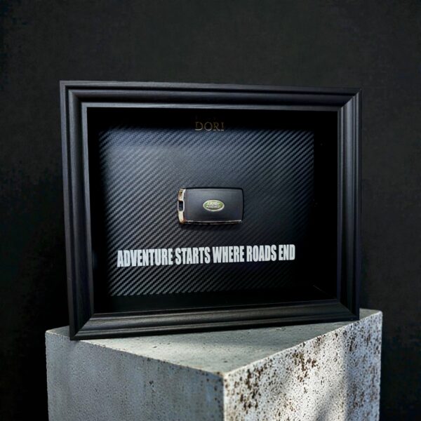 Automobilio raktelio dekoratyvinis paveikslas su anglies pluošto fonu ir užrašu „Adventure Starts Where Roads End“