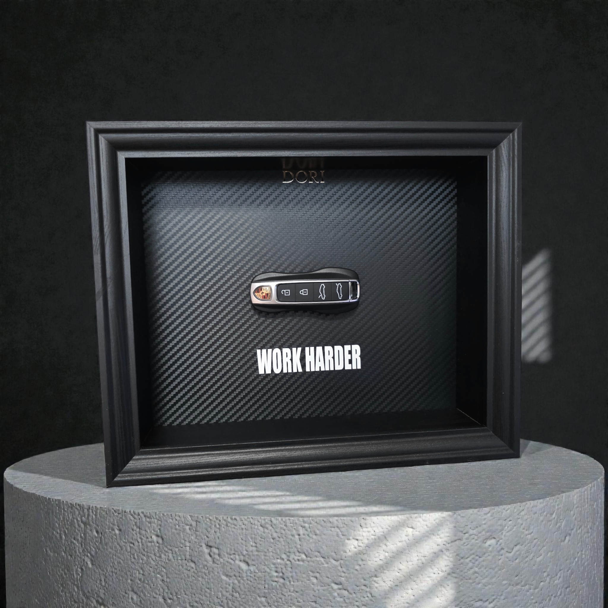 Automobilio raktelio dekoratyvinis paveikslas su anglies pluošto fonu ir užrašu „Work Harder“