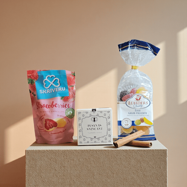 DORI saldžių skanėstų rinkinys su braškėmis šokolade, vaisių želė saldainiais ir pakuotu sausainiu, fotografuotas šiltame minimalistiniame fone.