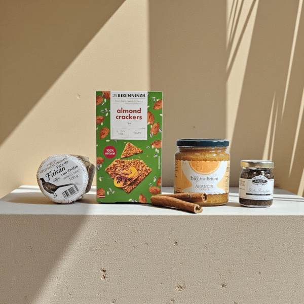 DORI gurmaniškas rinkinys su migdolų trapučiais, apelsinų džemu, trumų pagardu ir fazano paštetu, fotografuotas šiltame minimalistiniame fone.