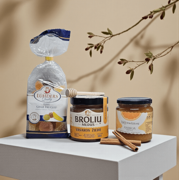 DORI gurmaniškas rinkinys su vaisiniais želė saldainiais, Brolių medumi ir apelsinų džemu, dekoruotas cinamono lazdelėmis ir šakelių elementais šiltame minimalistiniame fone.