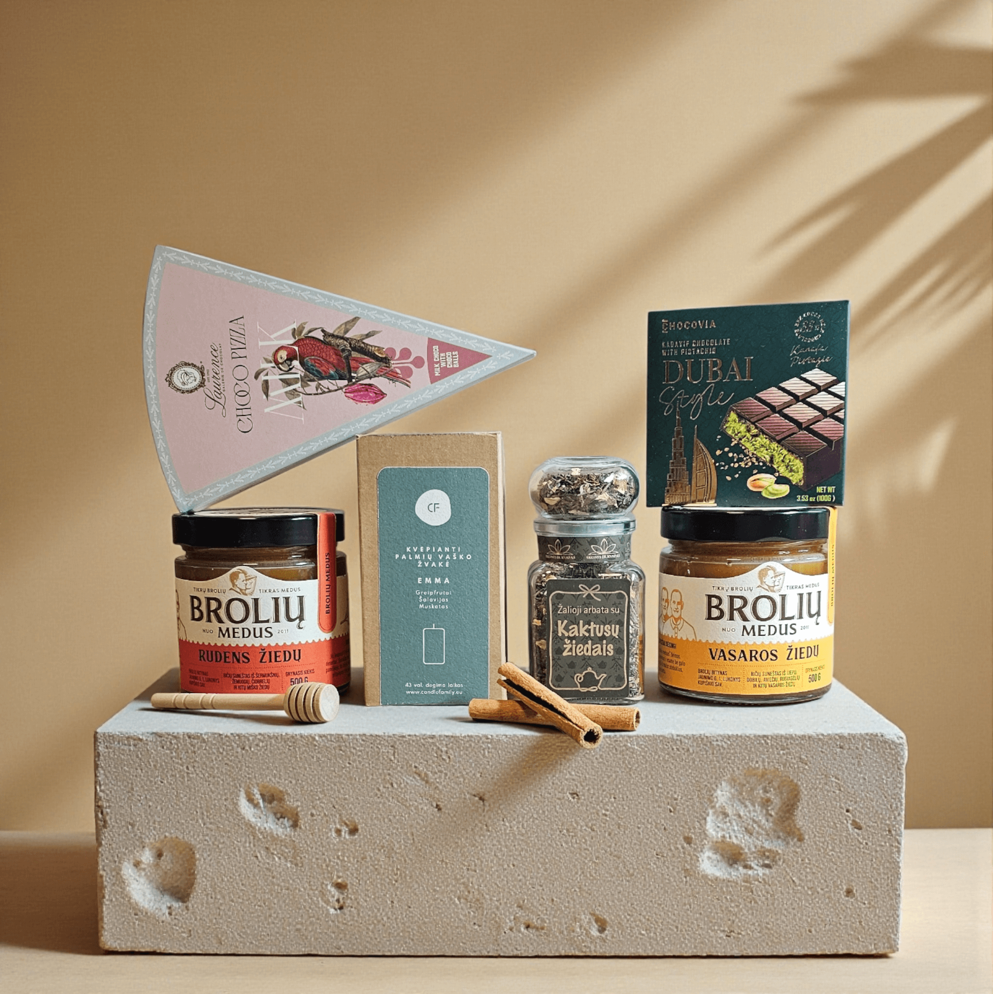 DORI gurmaniškas rinkinys su medumi, kakavos arbata, šokoladu ir arbata, fotografuotas natūraliame šiltame fone su cinamono lazdelėmis.