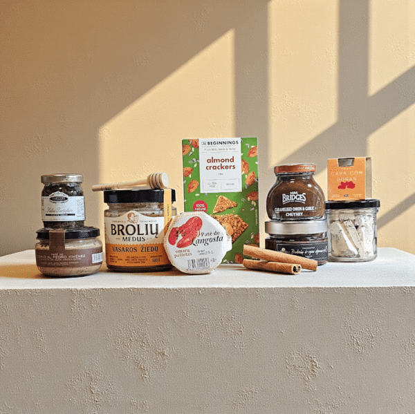 DORI gurmaniškas rinkinys su medumi, padažais, paštetais ir riešutų pagardais, fotografuotas šiltame fone su faktūrine platforma.