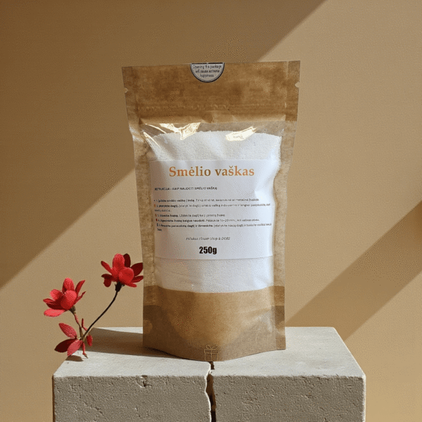 Birus smėlio vaškas 250 g kraft maišelyje su etikete, nufotografuotas šiltame minimalistiniame fone su dekoratyvine gėle.