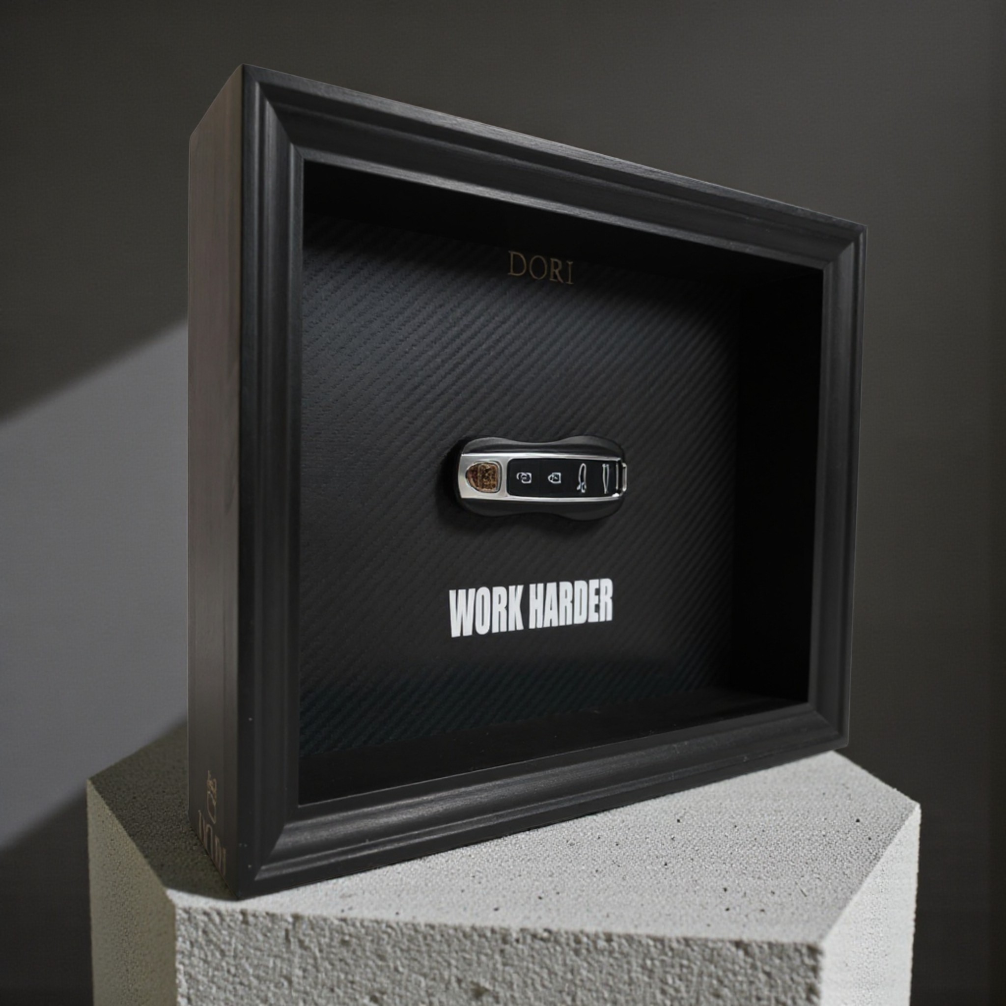 Automobilio raktelio dekoratyvinis paveikslas su anglies pluošto fonu ir užrašu „Work Harder“