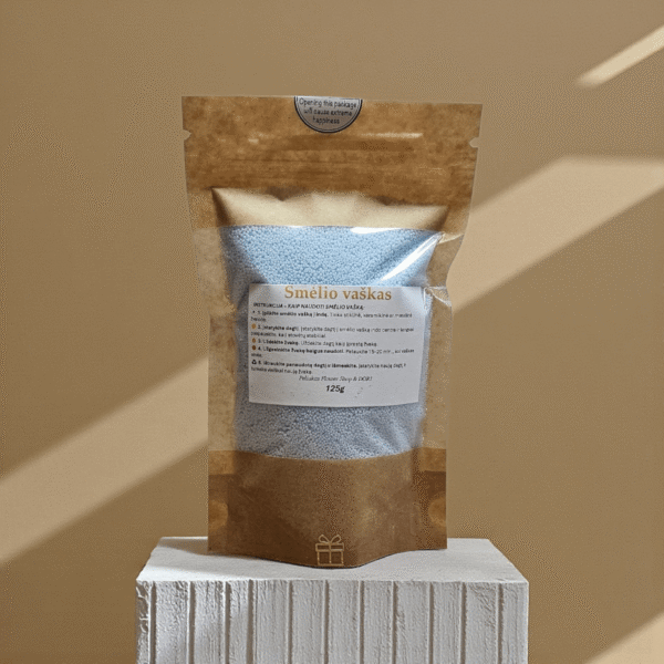 Žydras birus smėlio vaškas 125 g kraft maišelyje, pastatytas ant baltos faktūrinės pakylos, fotografuotas šiltame minimalistiniame fone su krintančiais šešėliais.