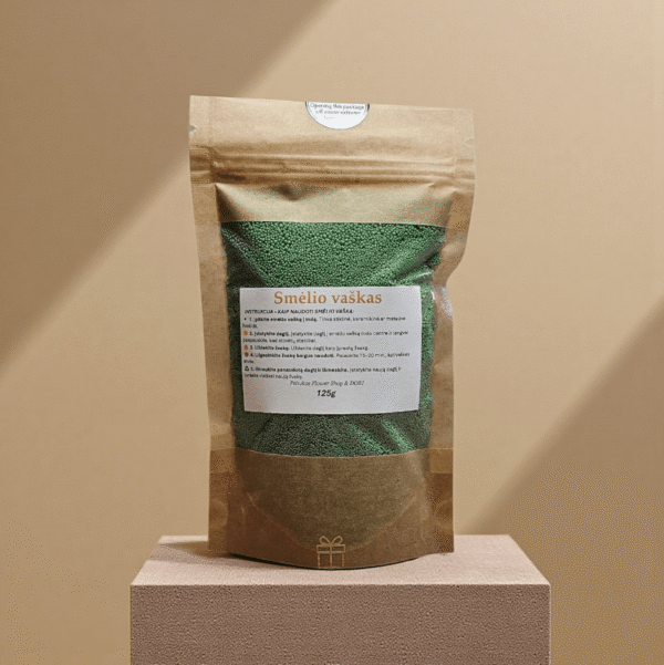 Žalias birus smėlio vaškas 125 g kraft maišelyje, stilingai fotografuotas ant faktūrinės pakylos šiltame minimalistiniame fone.