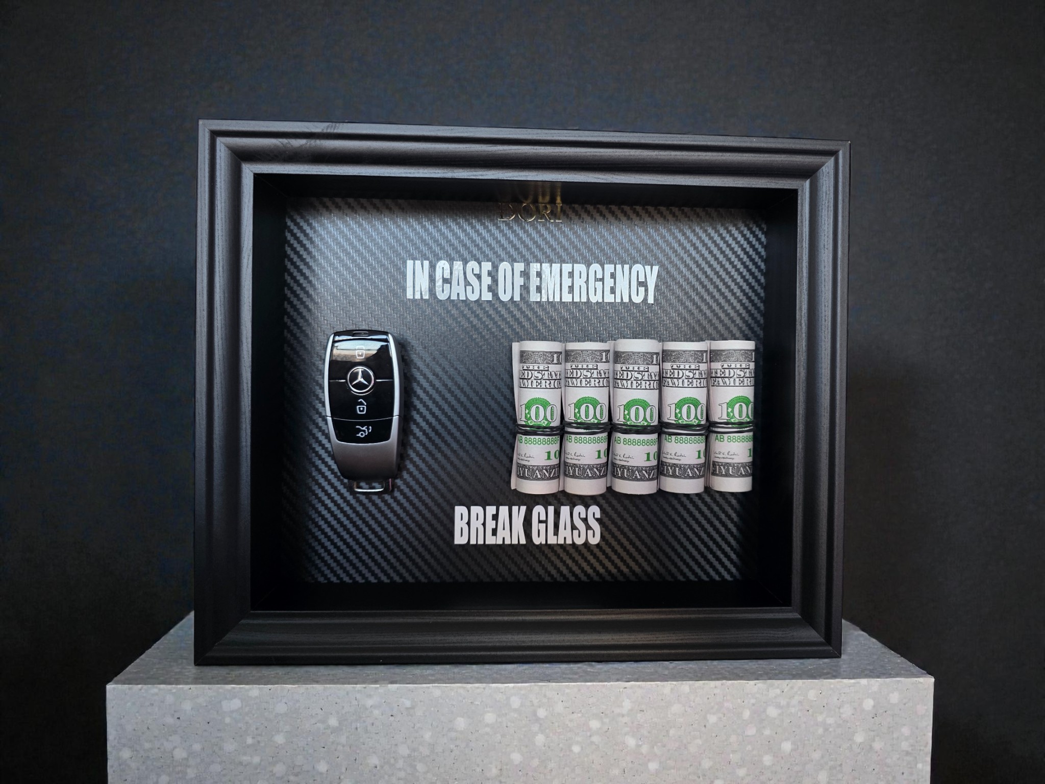 BREAK GLASS paveikslas su Mercedes-Benz automobilio raktu, juodu rėmu ir dekoratyviniais banknotų rulonais