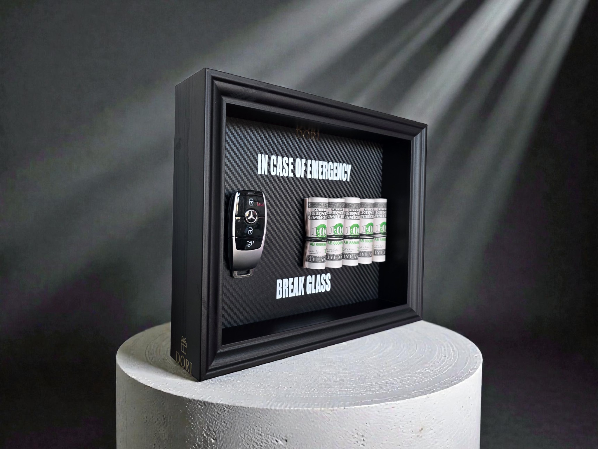 BREAK GLASS paveikslas su Mercedes-Benz automobilio raktu, juodu rėmu ir dekoratyviniais banknotų rulonais