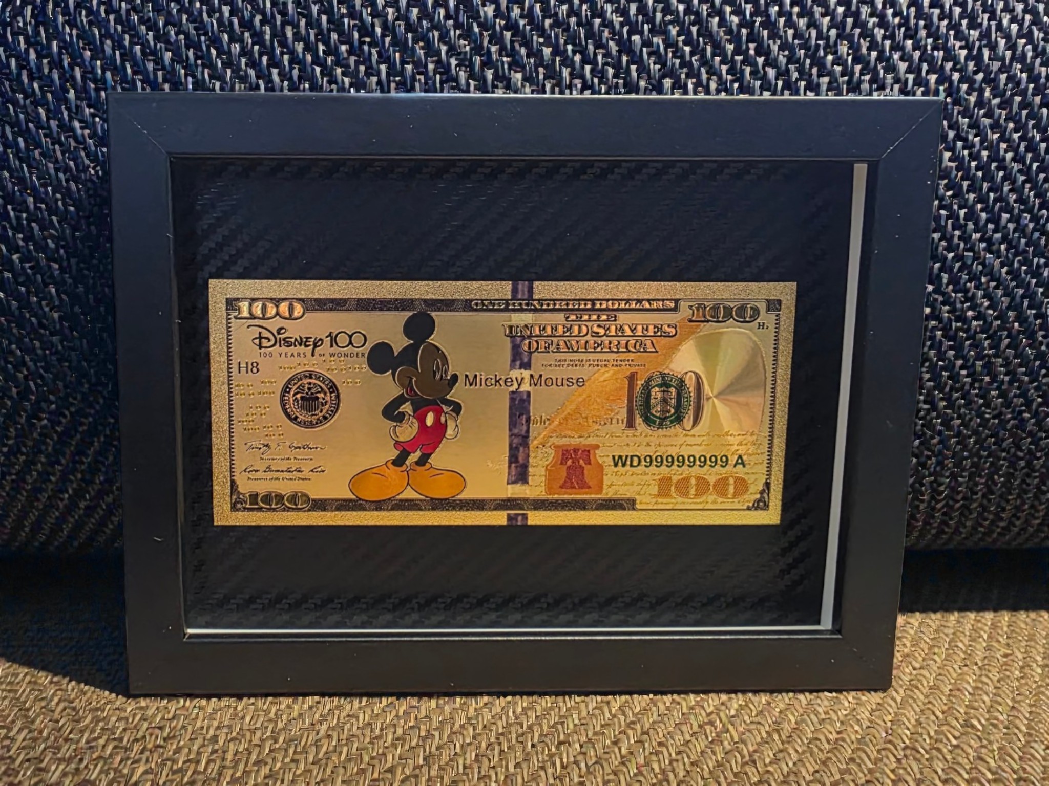 Auksinis 100 paveikslas su animacinio personažo motyvu juodame rėme