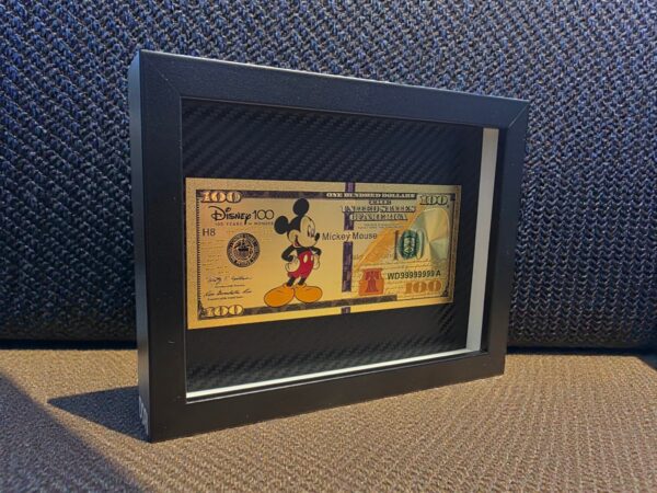 Auksinis 100 paveikslas su animacinio personažo motyvu juodame rėme