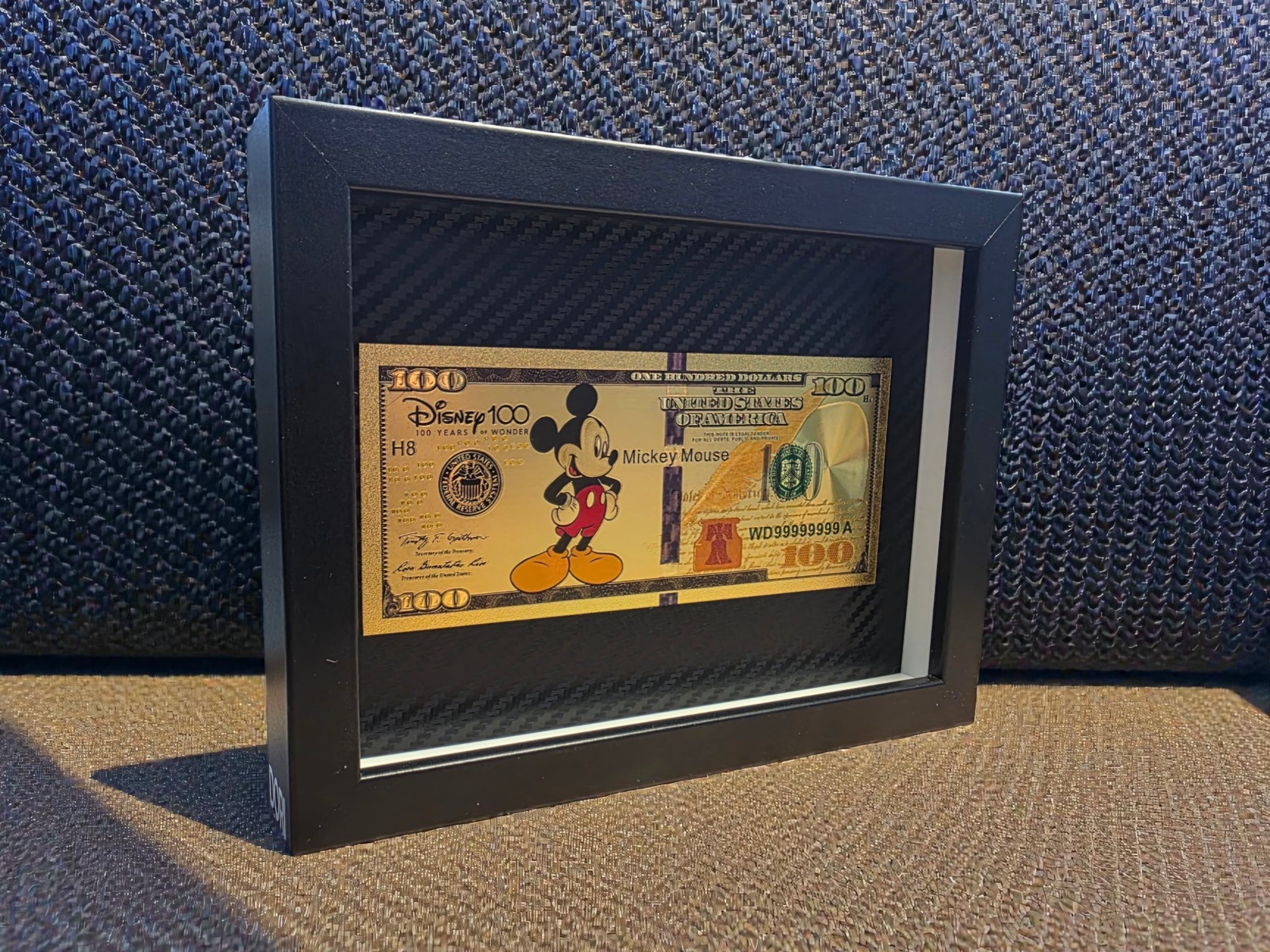 Auksinis 100 paveikslas su animacinio personažo motyvu juodame rėme