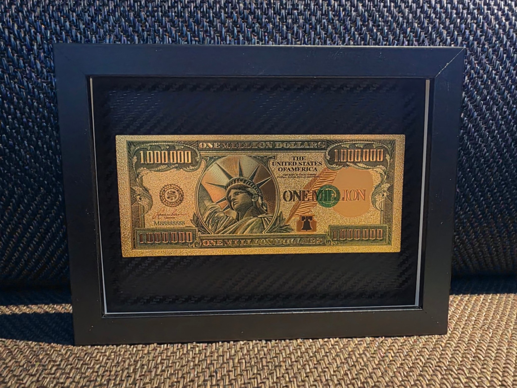 Auksinis ir žalias „One Million“ paveikslas juodame rėme